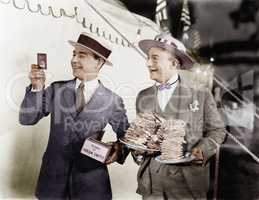 Man holding plates of sandwiches with a man looking at a film slide beside him