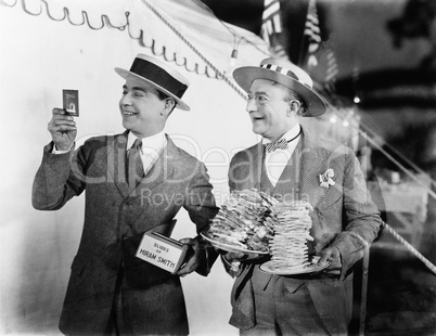 Man holding plates of sandwiches with a man looking at a film slide beside him