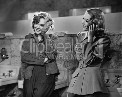 Two young women leaning against a bathroom sink and applying ice packs on to their faces