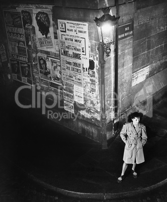 High angle view of a young woman waiting next to a lantern on a dark street corner