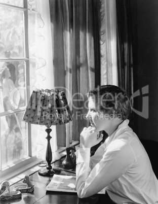 Profile of a young woman sitting at a desk and looking through a window