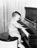 Profile of a little boy sitting on a stool and playing a piano