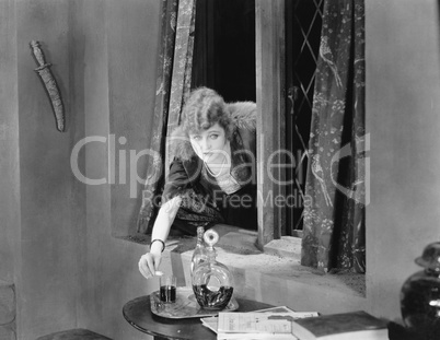 Portrait of a young woman reaching through a window and pouring poison into a glass