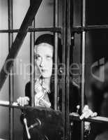 Young woman standing behind bars in a prison cell