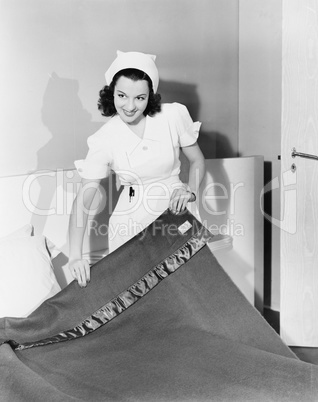 Female nurse making a bed in a hospital and smiling