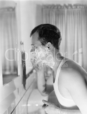 Profile of a young man in front of a mirror in a bathroom shaving