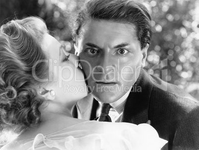 Close-up of a young man being kissed by a young woman and looking surprised