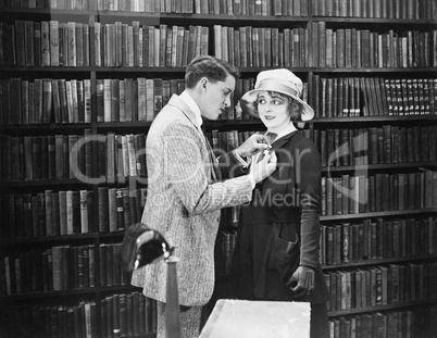 Profile of a young man attaching a brooch on a young woman's overcoat in a library