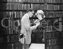 Profile of a young man attaching a brooch on a young woman's overcoat in a library