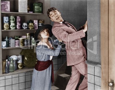 Profile of a young woman pushing out a young man from a domestic kitchen