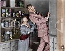 Profile of a young woman pushing out a young man from a domestic kitchen
