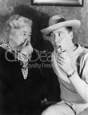 Young man smoking a pipe with a woman holding her nose