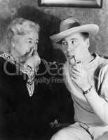 Young man smoking a pipe with a woman holding her nose