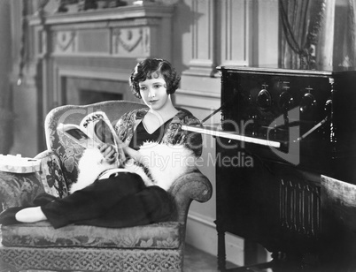 Young woman sitting in an armchair reading a magazine next to a radio