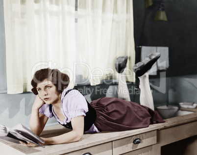 Young woman lying on a kitchen counter holding a book and thinking