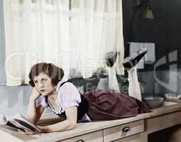 Young woman lying on a kitchen counter holding a book and thinking
