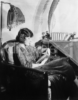 Profile of a young woman sitting in an armchair and reading a book