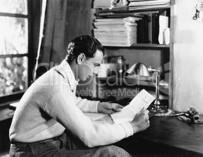 Profile of a young man reading a paper at his desk