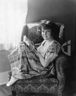 Portrait of a young woman sitting in an armchair and holding a book