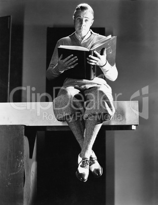 Portrait of a man sitting on a wooden plank and holding a book