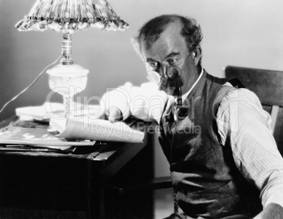 Profile of a man sitting at a desk and holding a book and smoking a pipe