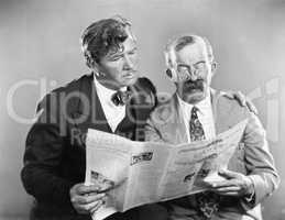 Two mature men reading a newspaper together