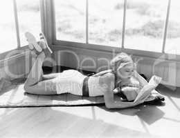 Profile of a young woman lying on a blanket on her stomach and reading a book