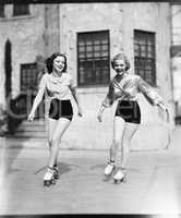 Two young women roller skating on the road and smiling
