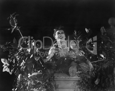 Portrait of a young man sitting on a wall with lowers and plants and smiling
