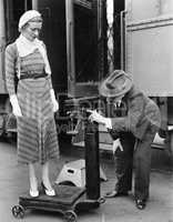 Profile of a man measuring weight of a woman standing on a weighing scale in front of a train