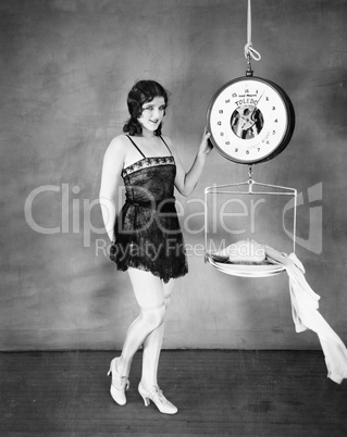 Portrait of a young woman weighing her clothes on a weighing scale