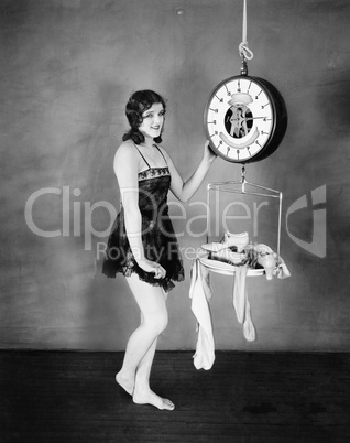 Portrait of a young woman weighing her clothes and sandals on a weighing scale