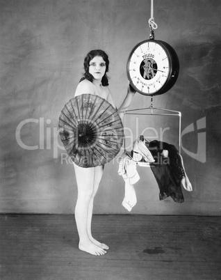 Portrait of a young woman standing in front of a weighing scale and hiding herself with a parasol
