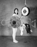 Portrait of a young woman standing in front of a weighing scale and hiding herself with a parasol