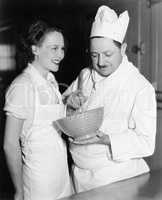 Profile of a chef stirring a mixture in a bowl and a young woman standing beside him