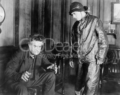 Man sitting on a couch explaining something with his hands to a young man in front of him