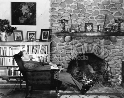 Profile of a young man resting in an arm chair near a fireplace