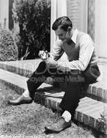 Young man sitting on a step and holding a cigarette lighter with a pipe
