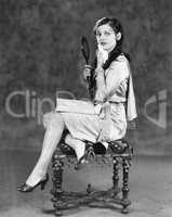 Young woman sitting on a stool holding a vanity mirror