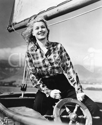 Young woman standing at the helm of a sailboat and holding the wheel