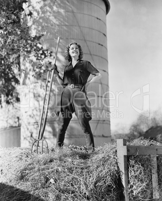Young woman standing on a haystack and holding a pitchfork
