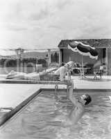 Young woman lying on a diving board with a young man hanging from it