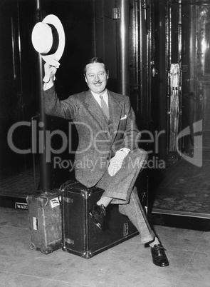 Portrait of a businessman sitting on his suitcases on a platform in front of a train