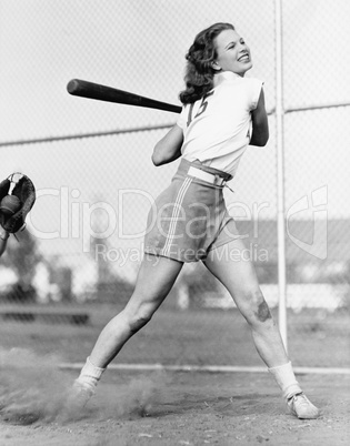 Young woman swinging a baseball bat in a baseball field
