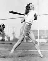 Young woman swinging a baseball bat in a baseball field
