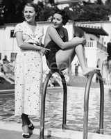 Profile of a young woman sitting on a ladder at the pool side with another woman standing behind her