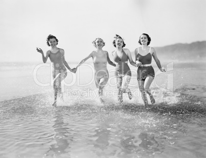 Four women running in water on the beach