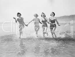 Four women running in water on the beach