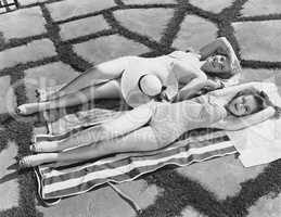 High angle view of two young women lying on a towel in the sun