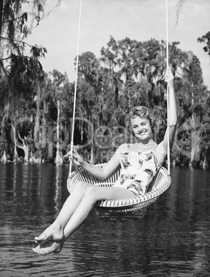 Portrait of a young woman sitting on a swing at the lakeside and smiling